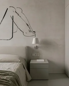 A minimalist bedroom featuring a bed with light-colored bedding, a concrete headboard, and a bedside table with a lamp.