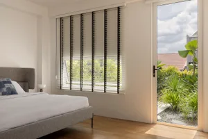 A minimalist bedroom featuring a bed with white sheets, a gray upholstered headboard, and a window with white mini blinds and