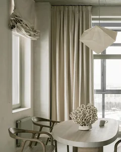 A minimalist dining room with a round wooden table, a concrete floor, and paper lampshade.