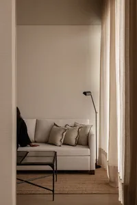 A cozy minimalist living room featuring cushions on a sofa, a floor lamp, and a glass-top coffee table.