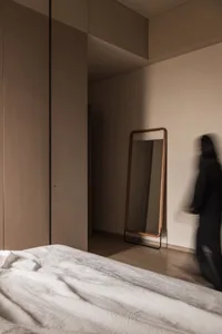 A modern bedroom featuring white bedding on a wooden floor with a wooden-framed mirror leaning against the wall.