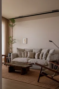 A modern living room featuring beige fabric, plush cushions, a wooden coffee table, and a tall potted plant.