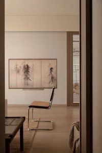 A modern living room featuring a wooden dining table with chairs, a bonsai tree, and sheer curtains allowing natural light to