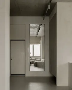 A minimalist living room with concrete walls and floor, featuring a large mirror reflecting the interior.