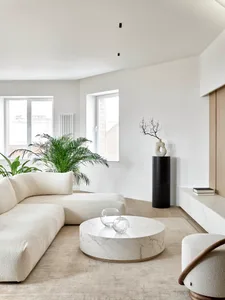A modern living room with a white marble coffee table, white corner sofa, and green plants.