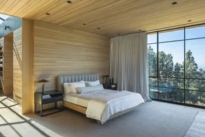 Modern bedroom featuring a minimalist design with wooden walls and a large window showcasing a scenic view.