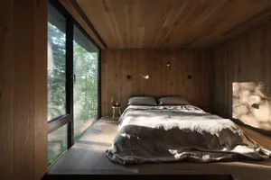 Minimalist bedroom with wooden walls, floors, and ceiling, featuring a bed with gray sheets and a small nightstand with a pla