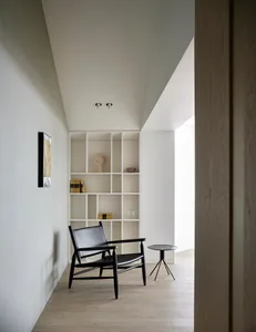 Modern minimalist home entry with a black armchair, white shelving unit, and wooden floor.