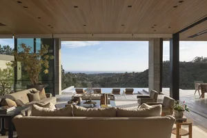 Modern patio with minimalist design featuring wooden and glass panels and concrete elements, overlooking a scenic hillside.