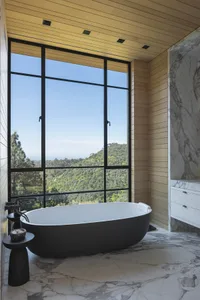 Modern bathroom featuring a freestanding bathtub with a view of the mountains, surrounded by marble and concrete materials.