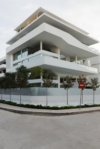 Modern multi-story building with white concrete and green foliage.