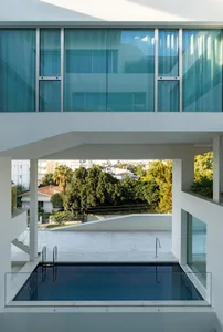 Modern building with glass walls and a rooftop pool overlooking greenery.