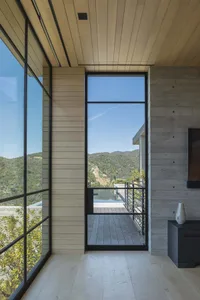 A modern interior with a wooden wall and large glass door leading to a wooden deck overlooking a scenic landscape.