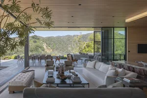 A modern living room featuring wood, glass, fabric, and concrete materials, with comfortable seating and a large window overl