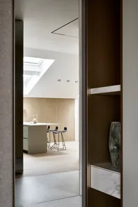 Modern minimalist kitchen with a wooden island, black stools, and a skylight.
