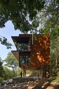 A modern treehouse with wooden siding and large windows surrounded by trees.
