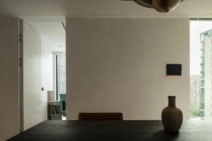 Minimalist dining room featuring dark wood table and modern chair against a plain wall and large window.