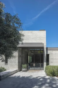 Concrete and glass modern house exterior with large windows and greenery.