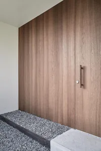 A modern front entry featuring a wooden door and gravel pathway.