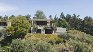 A modern residence with a concrete exterior surrounded by lush greenery and trees.
