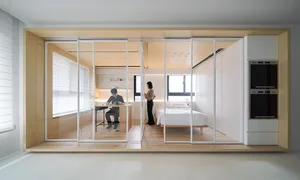 A minimalist bedroom with wood finishes and metal accents, featuring a white bed and a person standing near a window.