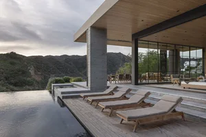 An outdoor residential deck featuring modern design elements such as concrete, glass, and wood, with an infinity pool and lou