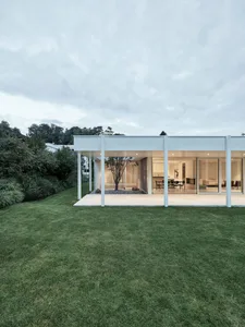 Modern residential building with glass walls and a green lawn.