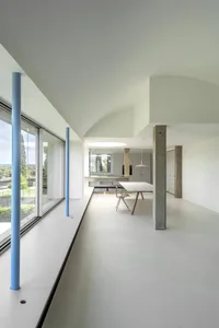 Modern minimalist living room with concrete walls and floor, large windows, and simple furniture.