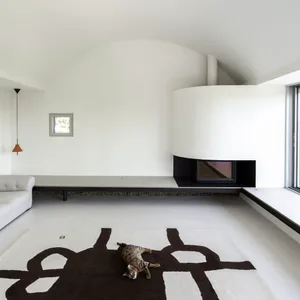 A modern minimalist living room with a concrete floor, featuring a white curved wall with a built-in fireplace, a white sofa,
