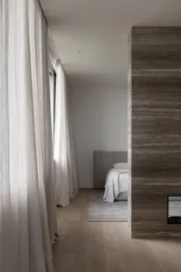 Interior shot of a minimalist bedroom featuring concrete walls, wooden flooring, and a bed with a simple headboard and white 