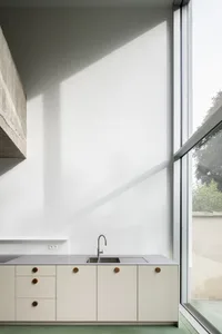 Modern kitchen featuring minimalist design with concrete walls and white cabinetry.