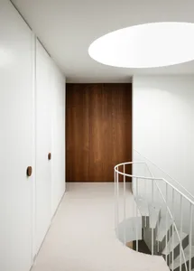 Spiral staircase with white railings and wooden walls in a minimalist interior.