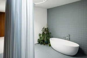 Modern bathroom with gray-tile walls and floor, concrete bathtub, and green plant.