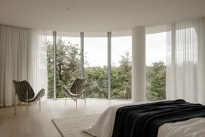 Modern bedroom featuring a glass-enclosed floor-to-ceiling window, wooden flooring, and fabric furniture.