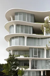 Modern apartment building with glass balconies and white columns against a cloudy sky.