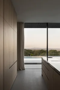 Modern kitchen with dark wooden cabinets and a large window offering a view of a pool and trees.
