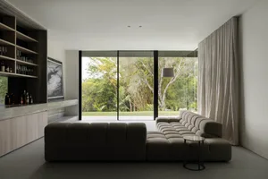 A modern living room with a fabric couch, a floor lamp, and a bar area with a glass countertop and shelves.