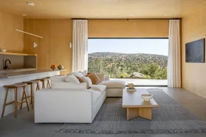 Minimalist living room with white sofa, concrete flooring, and large window overlooking landscape