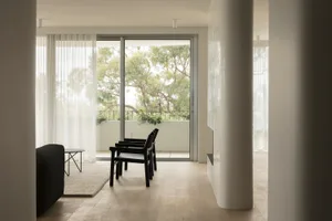 A modern minimalist living room with white walls, large glass windows, and wood flooring.