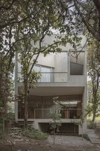 A modern, minimalist residence with a concrete exterior surrounded by lush greenery.