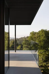 A modern residential patio with glass walls and a metal railing overlooking lush greenery.