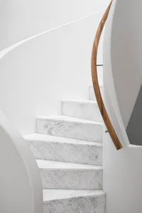 Modern, white marble stairs with a wooden handrail.