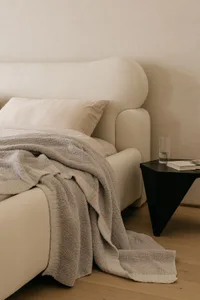 A minimalist bedroom with a white bed, grey blanket, and black side table.