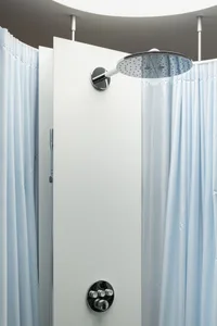 A minimalist shower enclosure with white curtains, featuring a metal shower head and glass elements.