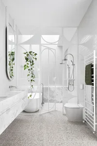 A modern bathroom featuring white terrazzo flooring and minimalist white fixtures, with a single potted plant and a large mir