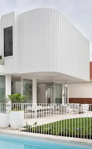 Modern exterior with white concrete poolside lounge area featuring curved structural design and white metal railings.