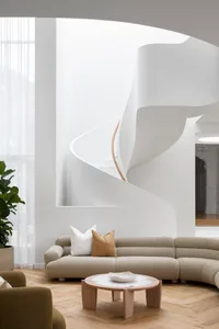 Modern living room with neutral-toned furniture and a curved staircase