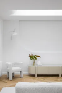 Modern, minimalist living room with white furniture and wooden flooring.