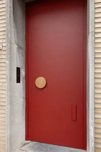 A sleek, red, metallic front door with a unique wooden circle handle.