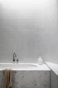 A modern bathroom featuring a tiled wall, marble base, and concrete elements.